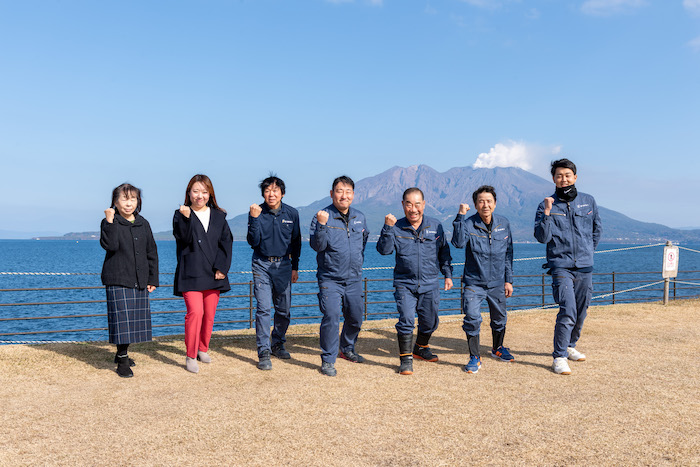 桜島を背景にガッツポーズをするスタッフ